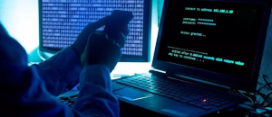 Hacker holding a phone infront of a laptop and monitor